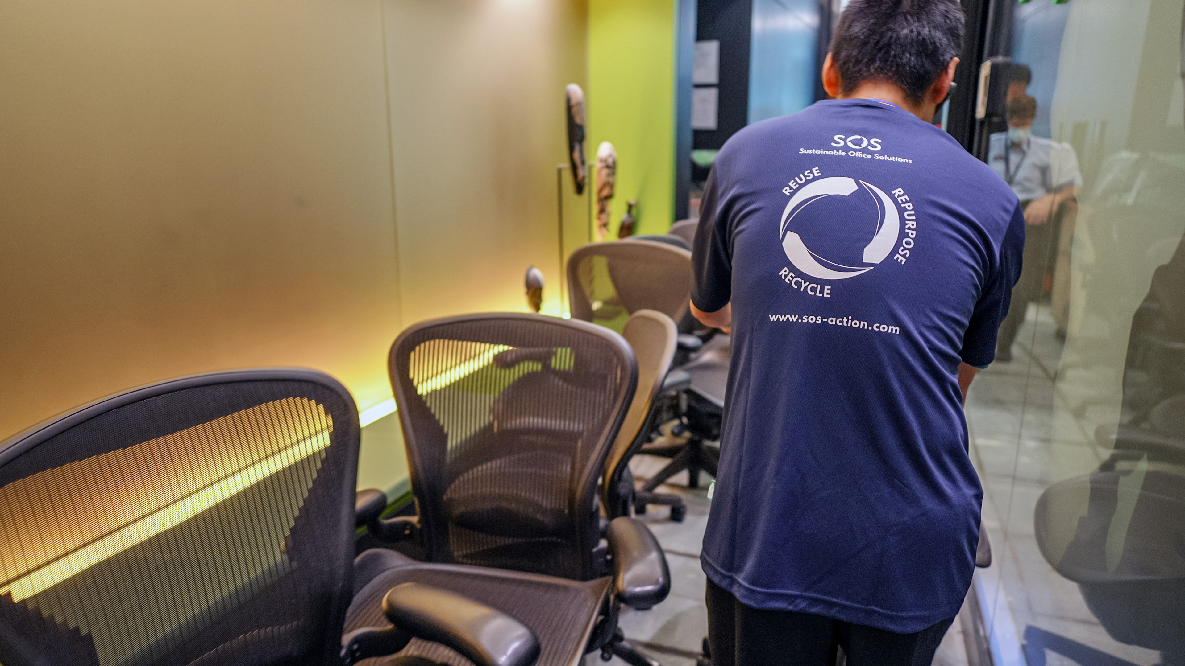 A SOS staff member inspects office chairs wearing a SOS tee-shirt